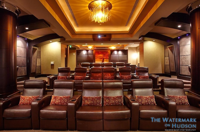 home theater room with a tray ceiling, arched walkways, and decorative columns