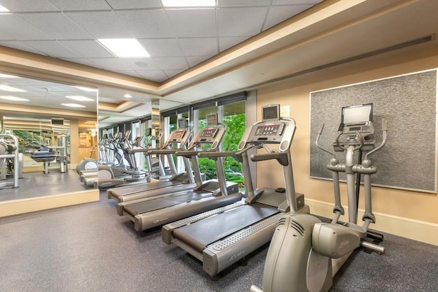 workout area with a tray ceiling, a drop ceiling, and baseboards
