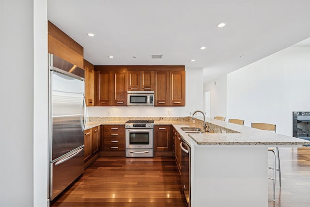kitchen featuring a peninsula, light stone counters, a sink, stainless steel appliances, and a breakfast bar area