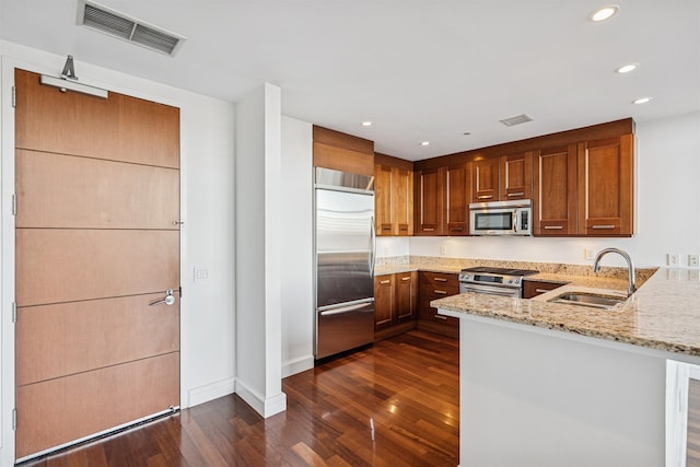 kitchen with a peninsula, visible vents, appliances with stainless steel finishes, light stone counters, and a sink