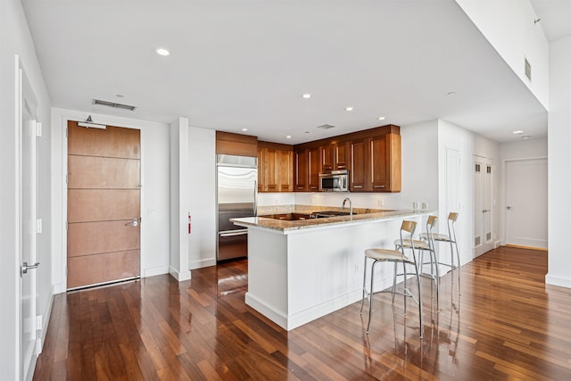 kitchen with a peninsula, visible vents, appliances with stainless steel finishes, dark wood-style flooring, and light stone counters