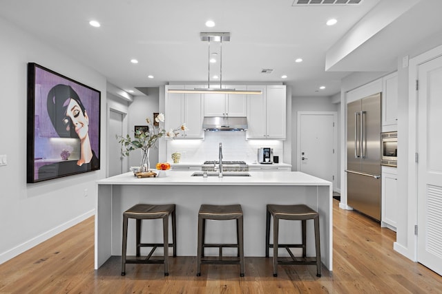 kitchen with a kitchen bar, backsplash, under cabinet range hood, and stainless steel appliances