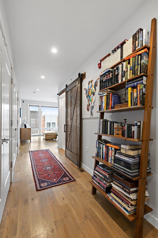 corridor featuring recessed lighting, wood finished floors, a barn door, baseboards, and french doors