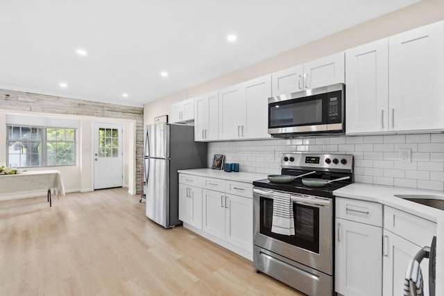 80 E 24th St, Bayonne, NJ 07002 - kitchen featuring stainless steel appliances, light countertops, light wood finished floors, decorative backsplash, and white cabinets