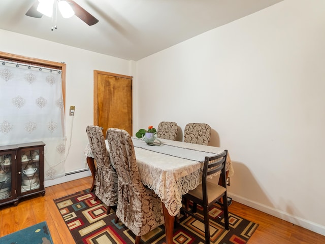 dining space featuring ceiling fan, a baseboard radiator, baseboards, and wood finished floors