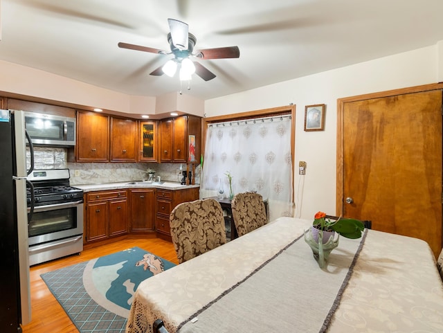 kitchen with light wood finished floors, backsplash, light countertops, brown cabinetry, and stainless steel appliances