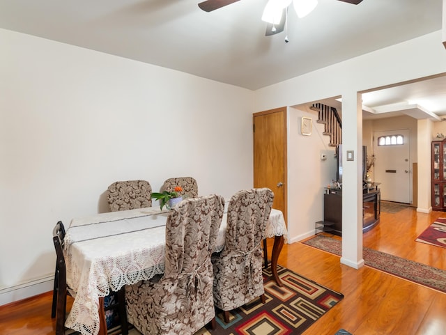 dining area featuring a baseboard heating unit, ceiling fan, baseboards, stairway, and light wood-style floors