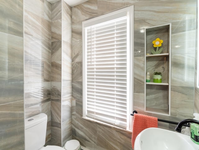 bathroom featuring toilet, tile walls, and a sink