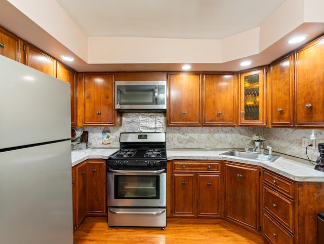 kitchen featuring tasteful backsplash, light countertops, appliances with stainless steel finishes, light wood-style floors, and a sink