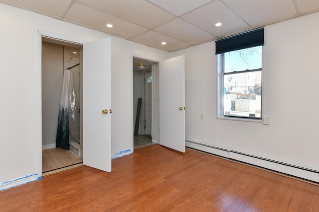 empty room with a paneled ceiling, baseboard heating, wood finished floors, and recessed lighting