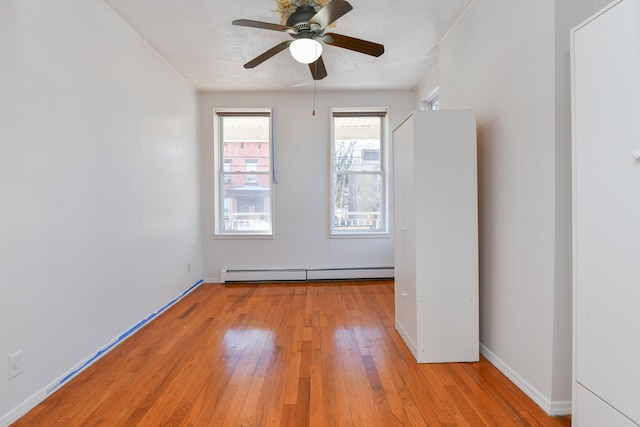 empty room with a baseboard heating unit, light wood-style floors, baseboards, and a ceiling fan