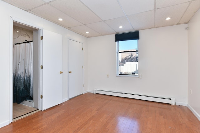 empty room with baseboards, a drop ceiling, a baseboard radiator, wood finished floors, and recessed lighting