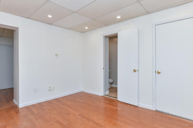 unfurnished bedroom featuring a paneled ceiling, recessed lighting, ensuite bathroom, wood finished floors, and baseboards