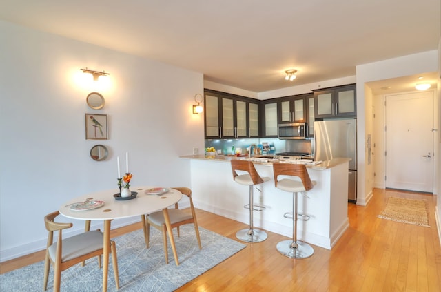 105 Greene St Unit 1101, Jersey City, NJ 07302 - kitchen featuring appliances with stainless steel finishes, light wood finished floors, a breakfast bar area, a peninsula, and glass insert cabinets