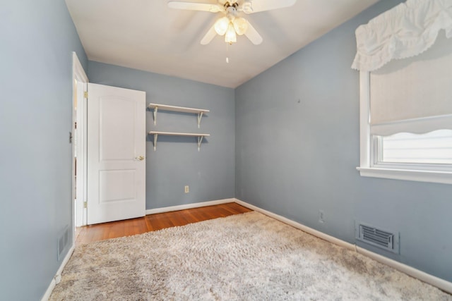 empty room with baseboards, a ceiling fan, visible vents, and wood finished floors