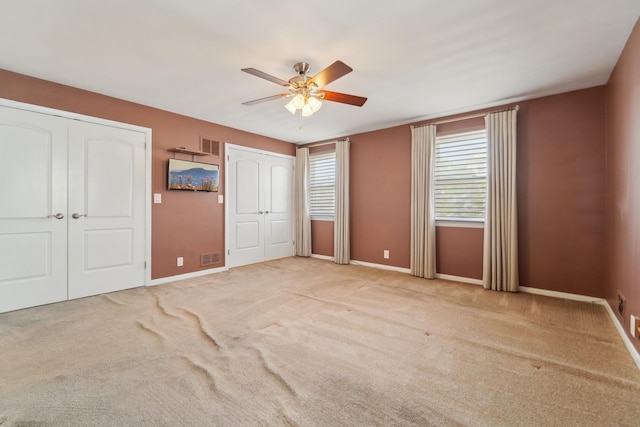 unfurnished bedroom with baseboards, ceiling fan, visible vents, and two closets