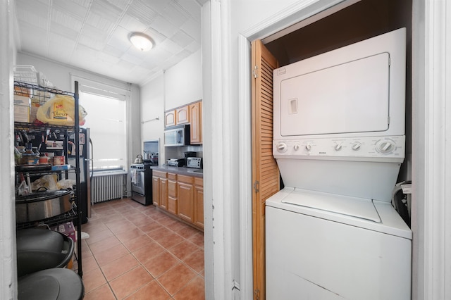 laundry area featuring radiator heating unit, stacked washer / dryer, and light tile patterned floors