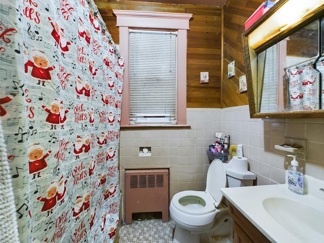 bathroom with radiator, walk in shower, toilet, vanity, and tile walls