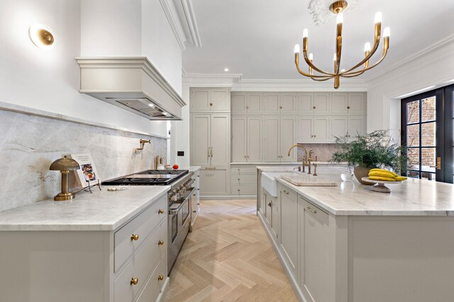 kitchen featuring gray cabinets, a chandelier, tasteful backsplash, a center island with sink, and arched walkways