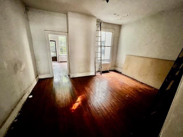 spare room with radiator heating unit, wood-type flooring, and a healthy amount of sunlight