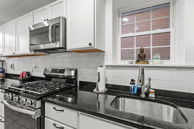 kitchen with sink, appliances with stainless steel finishes, dark stone countertops, backsplash, and white cabinets