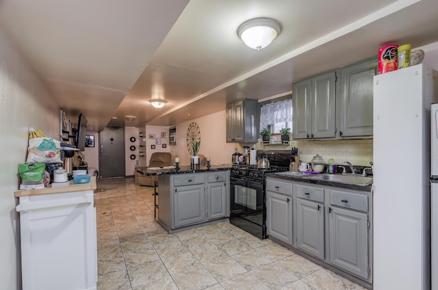 kitchen with dark countertops, gray cabinets, black range with gas cooktop, a sink, and a peninsula