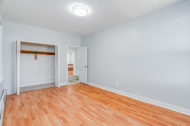 unfurnished bedroom featuring light wood finished floors, baseboards, baseboard heating, and a closet