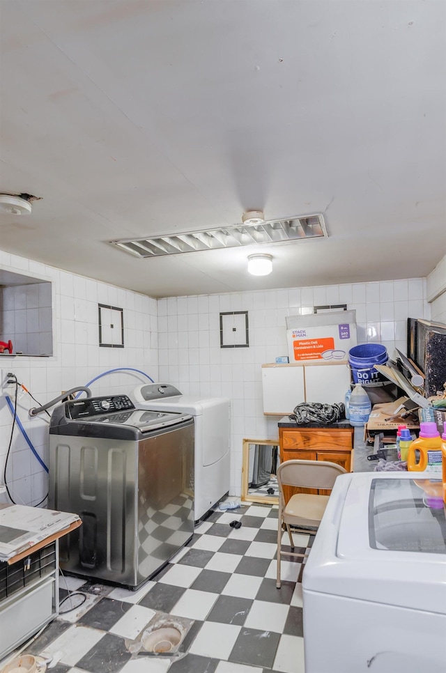 laundry room featuring a garage, laundry area, tile walls, tile patterned floors, and washer and clothes dryer