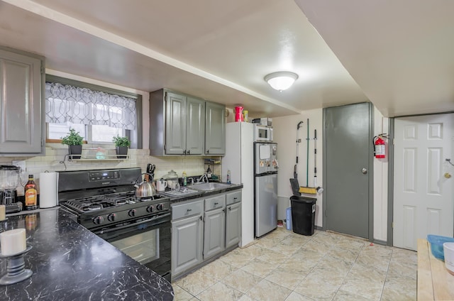 kitchen featuring black range with gas cooktop, tasteful backsplash, dark countertops, and gray cabinets