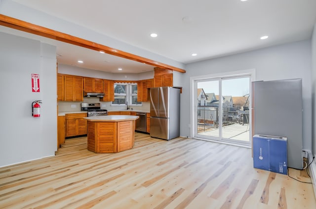 kitchen with light wood-style flooring, stainless steel appliances, light countertops, under cabinet range hood, and a sink