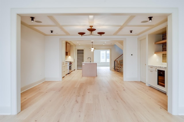 unfurnished living room with coffered ceiling, stairway, light wood-style floors, wine cooler, and a sink