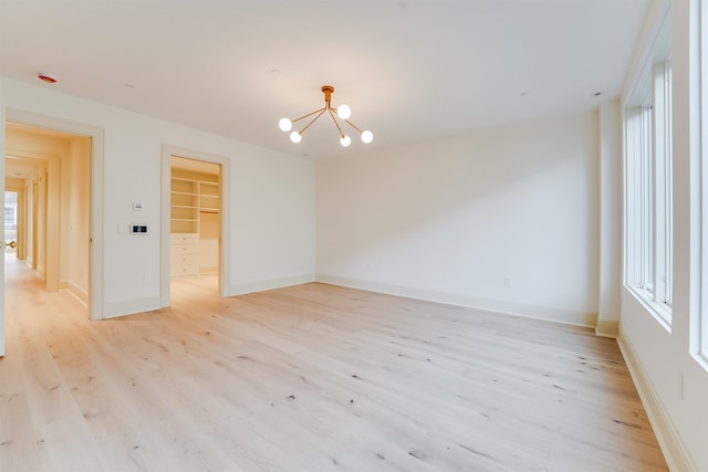 empty room with a chandelier, light wood-style floors, and baseboards