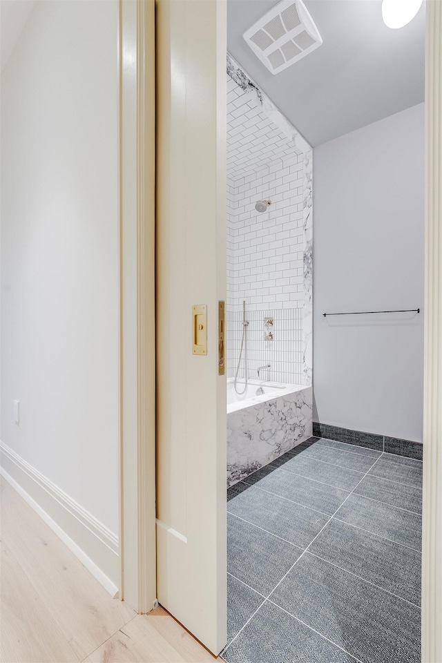 bathroom with a tub with marble appearance, visible vents, and baseboards