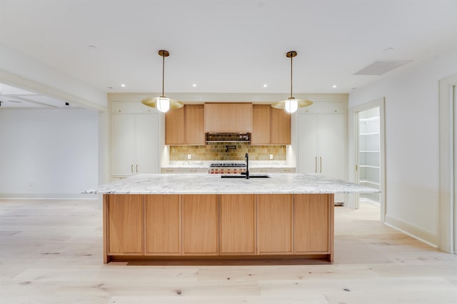 kitchen featuring backsplash, light stone countertops, light wood-style floors, a spacious island, and a sink