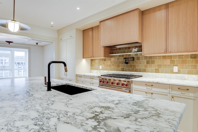 kitchen with stainless steel stove, light stone countertops, decorative backsplash, a sink, and hanging light fixtures