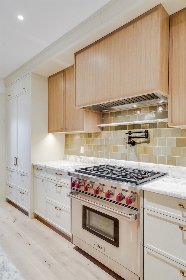 kitchen with tasteful backsplash, light brown cabinets, luxury stove, light wood-style flooring, and light stone counters
