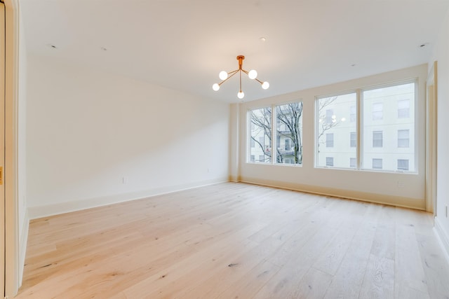 spare room with light wood finished floors, an inviting chandelier, and baseboards