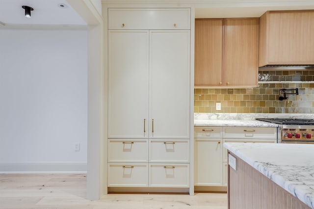 kitchen with stainless steel range, light stone counters, backsplash, and light wood-style flooring