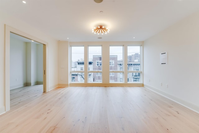 unfurnished room with recessed lighting, a view of city, light wood finished floors, and baseboards