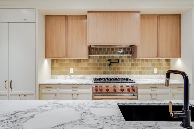 kitchen with high end range, light stone countertops, a sink, light brown cabinets, and backsplash