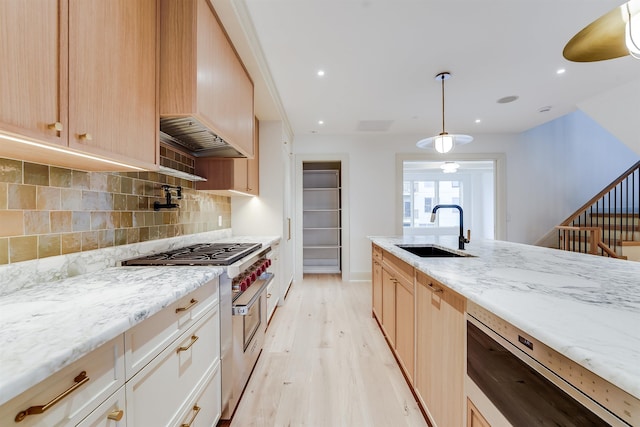 kitchen with a sink, light wood-style floors, high end stove, decorative backsplash, and light stone counters