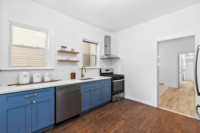 48 Armstrong Ave, Jersey City, NJ 07305 - kitchen featuring appliances with stainless steel finishes, wall chimney exhaust hood, blue cabinets, dark wood-type flooring, and tasteful backsplash
