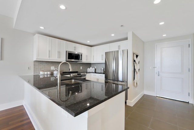 kitchen featuring white cabinets, kitchen peninsula, stainless steel appliances, and dark tile patterned flooring