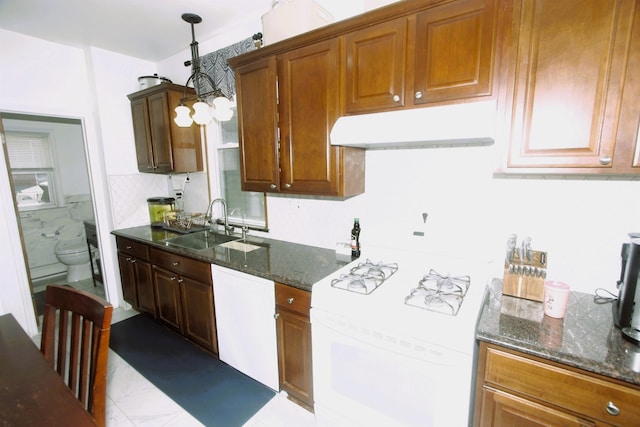 kitchen with white appliances, under cabinet range hood, a sink, dark stone counters, and brown cabinets