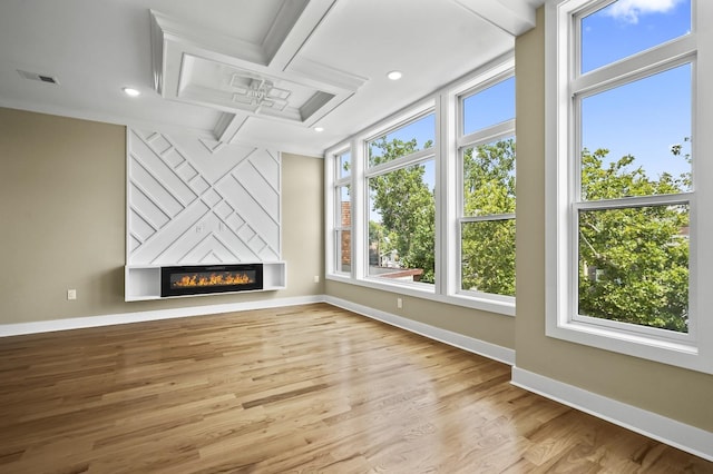 unfurnished living room featuring light wood-type flooring, a large fireplace, coffered ceiling, and a healthy amount of sunlight