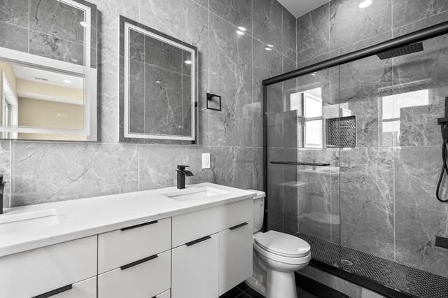 bathroom featuring tile walls, vanity, toilet, and a shower with shower door