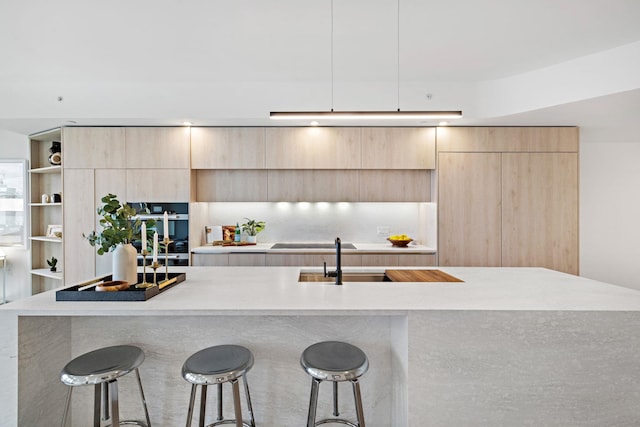 kitchen featuring a breakfast bar, a center island, black electric stovetop, sink, and light brown cabinetry