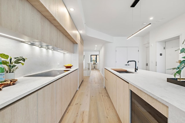 kitchen featuring sink, decorative light fixtures, black electric cooktop, light brown cabinetry, and light wood-type flooring