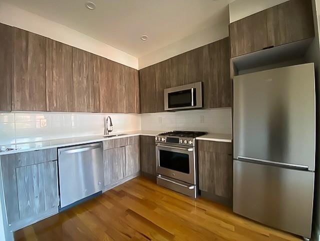 kitchen featuring tasteful backsplash, sink, appliances with stainless steel finishes, and light hardwood / wood-style flooring