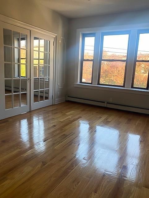 empty room featuring french doors, dark wood-type flooring, and a baseboard heating unit